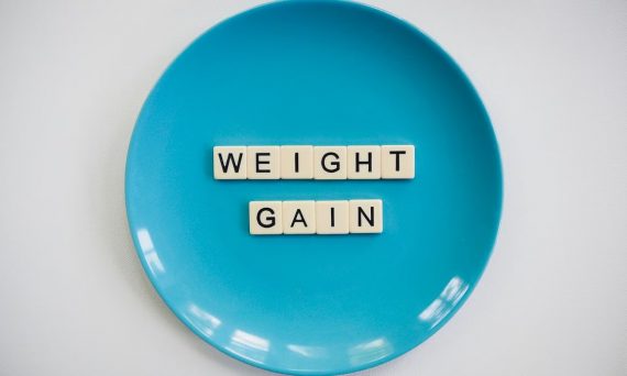 Scrabble tiles spelling 'weight gain' on a blue plate, symbolizing health and diet.