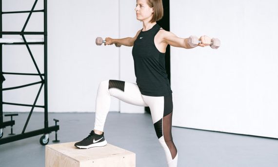 Woman performing fitness exercise with dumbbells in a gym setting, showcasing strength and balance.
